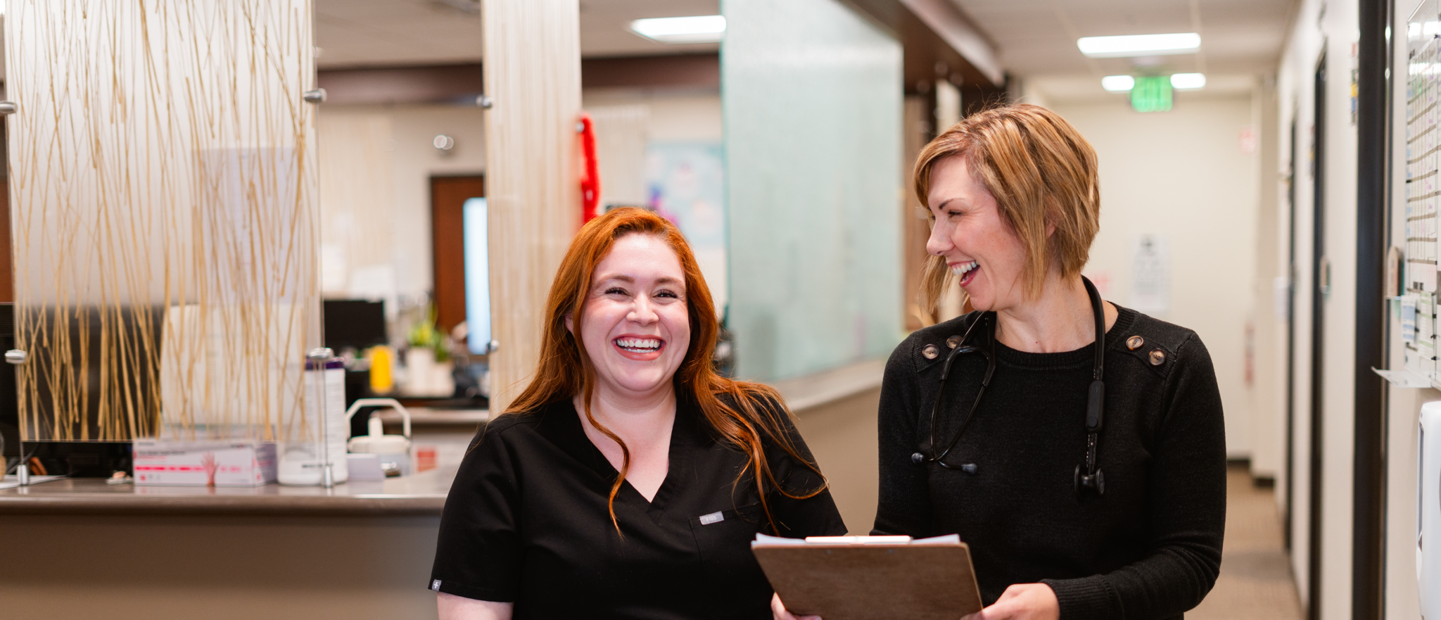 A doctor and medical assistant laugh while walking in hallway